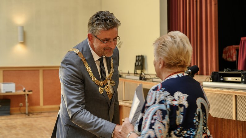 Ein Mann in Anzug und mit goldender Amtskette schüttelt einer Frau die Hand.